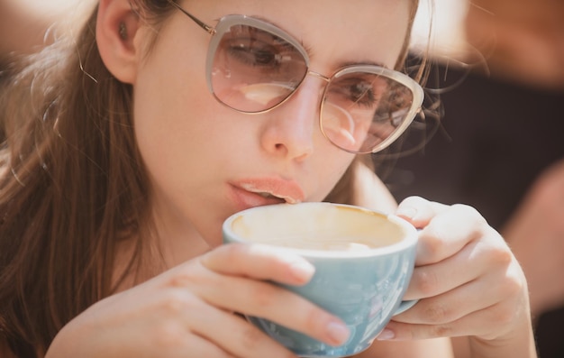 Feche o retrato de uma mulher com uma xícara de café. Mulher sensual tomando café ao ar livre.