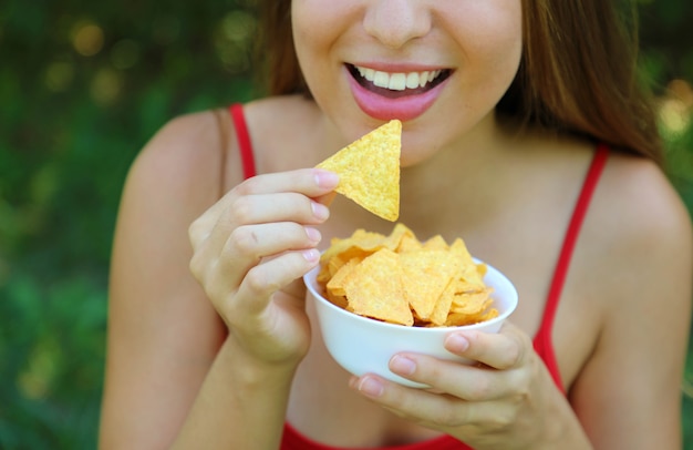 Feche o retrato de uma mulher comendo batatas fritas com uma tigela cheia na mão.