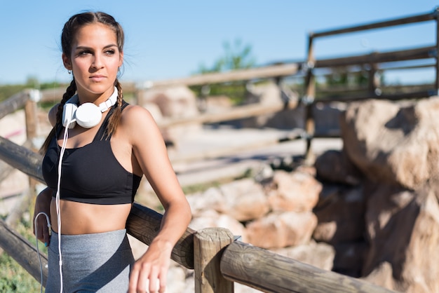 Feche o retrato de uma mulher fazendo esporte descansando ao ar livre, sorrindo e ouvindo música