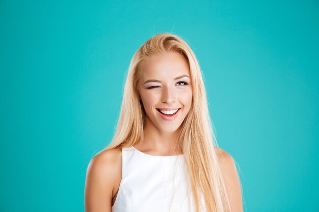 Feche o retrato de uma mulher loira sorridente, piscando e olhando para a frente, isolada na parede azul