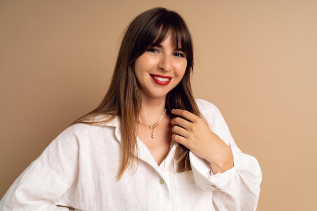 Foto feche o retrato de uma mulher morena na moda vestindo um terno de linho branco posando em fundo bege sorrindo um rosto bonito