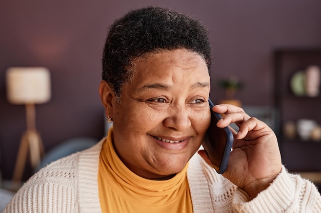 Feche o retrato de uma mulher negra sênior ligando por smartphone em casa e sorrindo alegremente