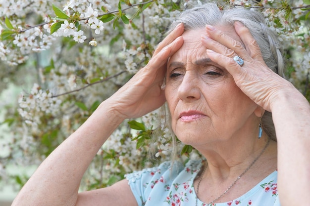 Feche o retrato de uma triste mulher sênior perto da árvore florescente da primavera