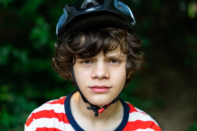 Feche o retrato do adolescente olhando para a câmera. Menino usando capacete de segurança para bicicleta, ao ar livre.