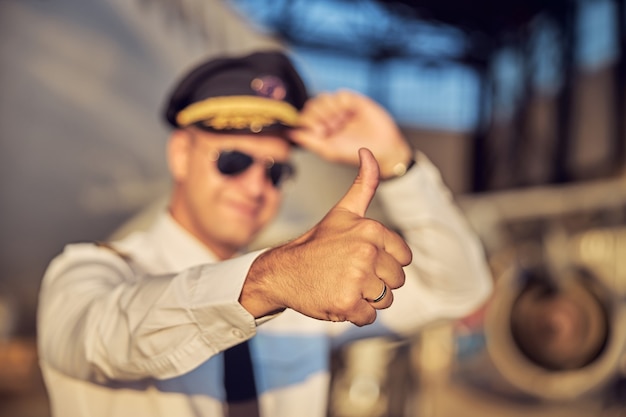 Feche o retrato do bonito piloto aparecendo em pé na frente de um avião de passageiros