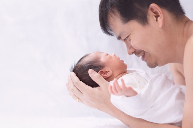 Foto feche o retrato do jovem pai asiático está segurando e olhando seu bebê com momento de felicidade.