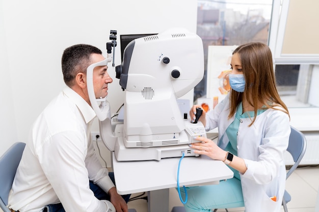 Feche o retrato do optometrista feminino usando a máquina do refratômetro enquanto testa a visão. paciente do sexo masculino na clínica.