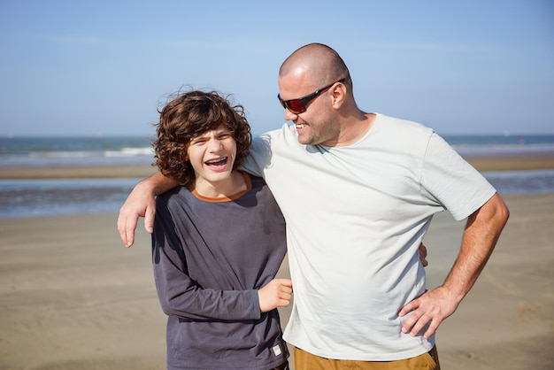 Feche o retrato do pai feliz e do filho adolescente no mar em roupas casuais Menino com aparelho dentário