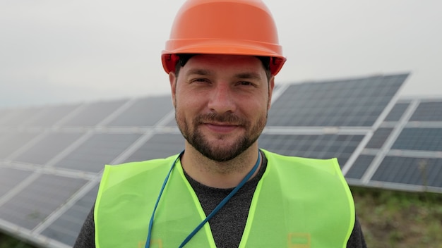 Feche o retrato do trabalhador elétrico masculino no capacete protetor em pé pelo painel solar. Produção de energia limpa. Energia verde. Fazenda solar ecológica.