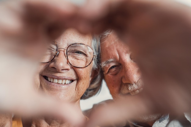 Feche o retrato feliz sincero casal de família aposentado de meia-idade fazendo gesto de coração com os dedos mostrando amor ou demonstrando sentimentos sinceros juntos dentro de casa olhando para a câmeraxA