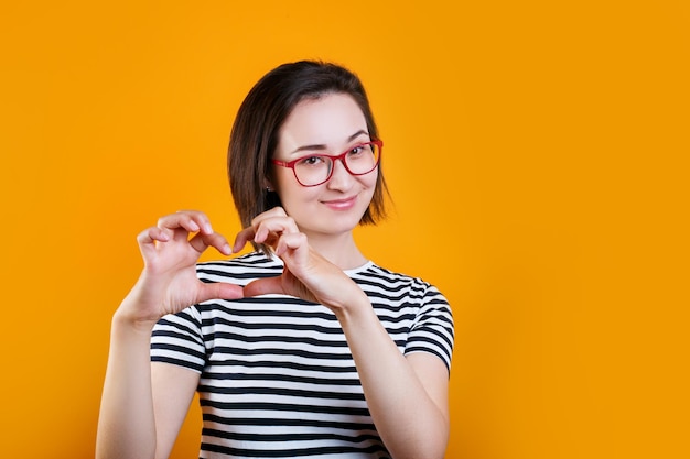 Feche o retrato fotográfico de uma linda e doce garota asiática dando-lhe seu coração isolado de fundo amarelo brilhante