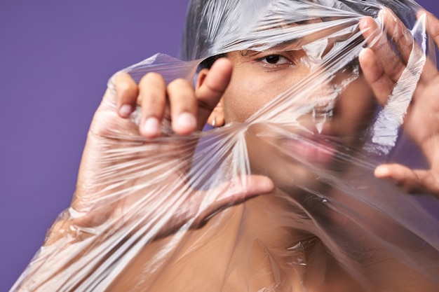 Feche o retrato horizontal de um jovem rasgando um saco plástico com olhos de olhar para a liberdade de transgênero