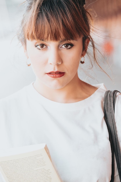 Feche o retrato Jovem ruiva olhando sério para a mulher de câmera hipster. Estação de trem Menina na moda em camiseta de verão e calça jeans preta. Mulher séria e pensativa posando na rua perto de uma parede de tijolos.