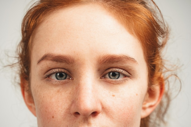 Feche o rosto de uma jovem com uma ruiva natural de olhos azuis assistir na câmera. Isolado sobre fundo branco.