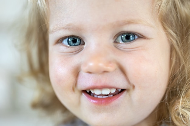 Feche o rosto de uma menina bonita com grandes olhos azuis, menina sorridente.