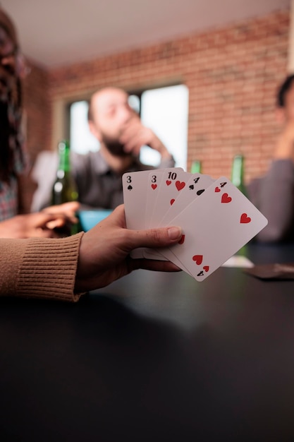 Feche o tiro da mão de uma mulher caucasiana segurando jogos de cartas enquanto desfruta de uma divertida atividade de lazer com os amigos. pessoa jogando jogos de cartas com as pessoas enquanto toma lanches e bebidas.