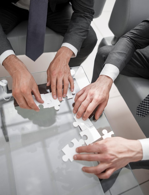 Feche os empresários montando um quebra-cabeça sentado atrás de uma mesa o conceito de cooperação