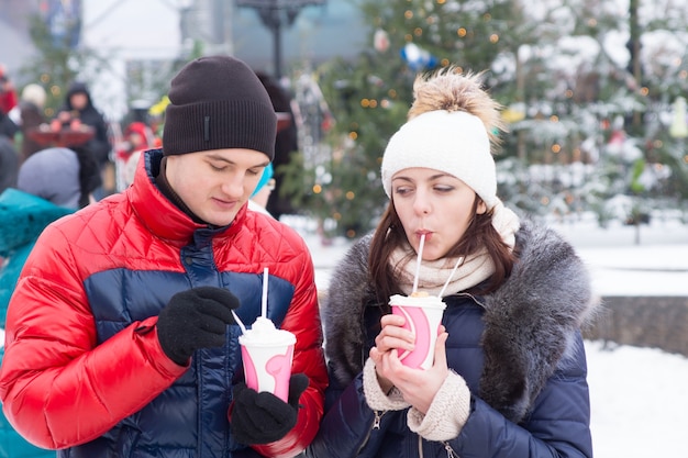 Feche os namorados jovens com bebidas de copo de inverno, tendo um encontro ao ar livre.