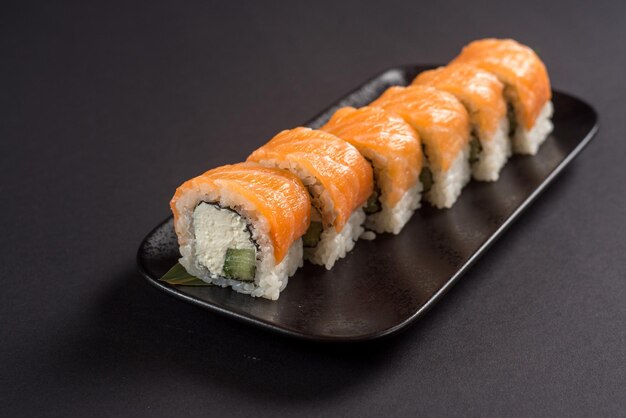 Feche os rolos de sushi em uma placa preta em fundo escuro