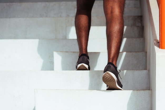 Feche os sapatos de atleta das pernas, corredor de esporte jovem, homem negro, correndo para subir escadas, fazendo exercícios de cardio esportivo na rua ao ar livre, exercício saudável antes do conceito de treino