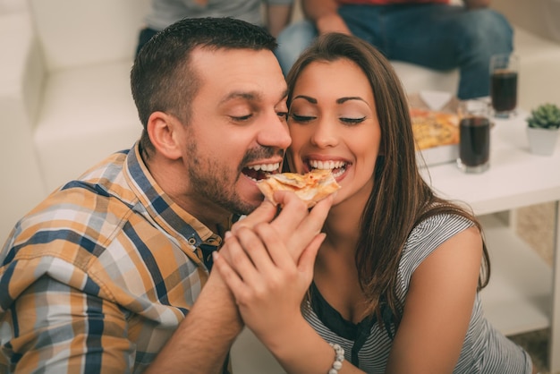 Feche-se de um jovem casal lindo compartilhando corte de pizza.