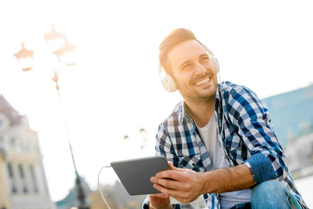 Feche-se de um jovem sentado ao ar livre ouvindo música. Ele está curtindo a música.