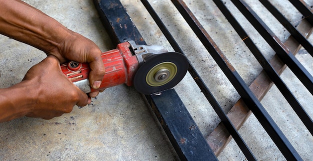 Feche, um homem que trabalha com rebarbadora. Conserto de portão de ferro