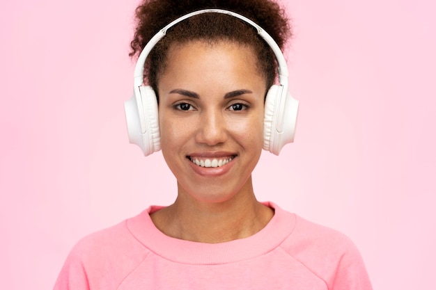 Feche uma mulher africana confiante em fones de ouvido sorrindo para a câmera isolada em fundo rosa pastel