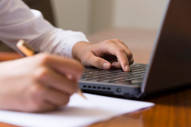 Feche uma mulher em uma caneta de camisa na mão trabalhando em um laptop e tomando notas