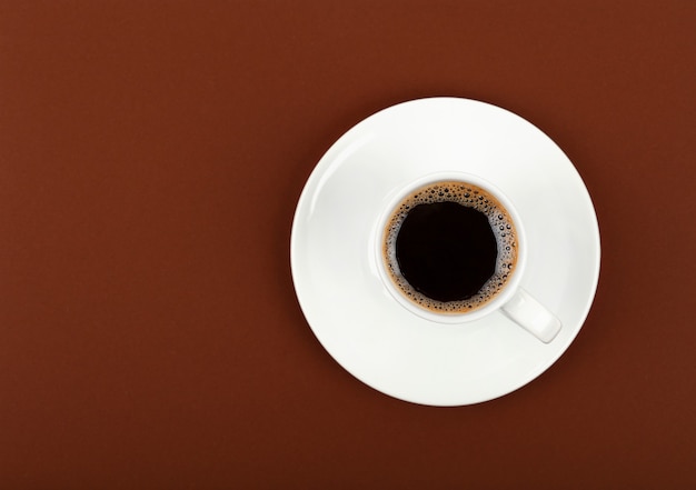 Feche uma xícara branca cheia de café preto em um pires sobre fundo de papel pardo, vista superior elevada, diretamente acima