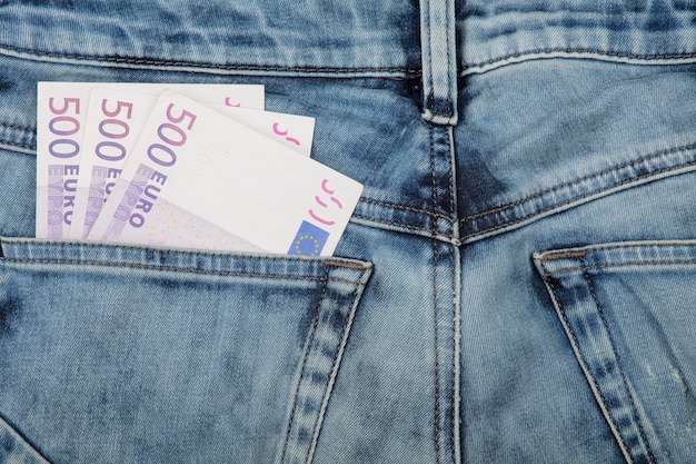 Feche várias cédulas de papel moeda de quinhentos euros no bolso traseiro da calça jeans, vista de ângulo baixo