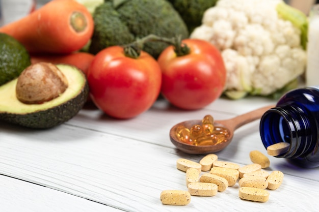 Foto feche vitaminas e suplementos em uma mesa de madeira branca com uma garrafa azul