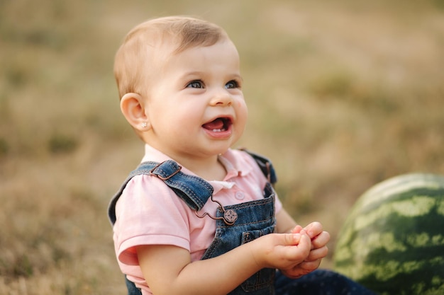 Fecho de uma adorável menina comendo melancia bebê estiloso em vestido jeans linda criança come frutas