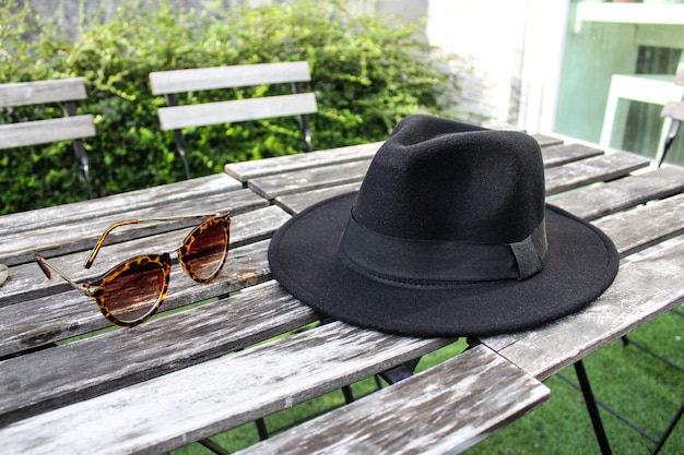 Fedora Hut und Sonnenbrille auf Holztisch im Freien