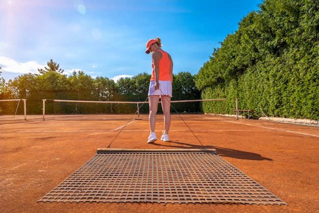 Fegen von orangefarbenem Ton auf einem Tennisplatz im Freien. junge Frau