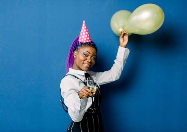 Feier-Konzept, Geburtstagsfeier - Nahaufnahme Porträt glückliche junge schöne afrikanische Frau in schwarzen Hosen und weißem Rock lächelnd mit buntem gelbem Partyballon. Blue Pastel Studio.