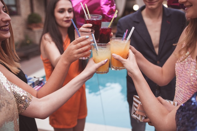 Feier-Party. Fröhliche Freundesgesellschaft mit Alkoholcocktails. Moderne Jugend mit Getränken im Fokus auf Vordergrundnahaufnahme. Alles Gute zum Geburtstag Toast, leckere Getränke, Glückwunschkonzept