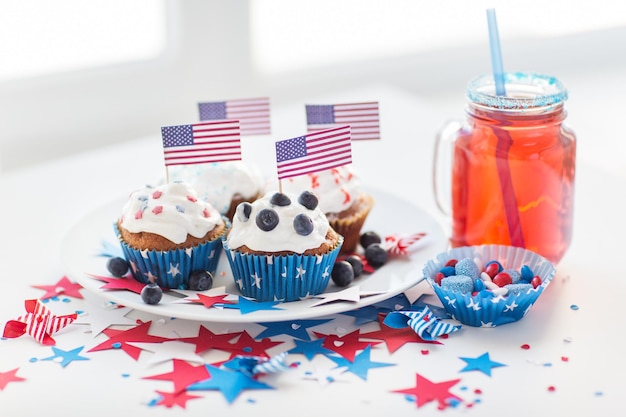 feier-, patriotismus- und feiertagskonzept - nahaufnahme von glasierten cupcakes, die mit amerikanischen flaggen, saftglas oder einmachglas, popcorn und süßigkeiten auf der party am 4. juli am unabhängigkeitstag dekoriert sind