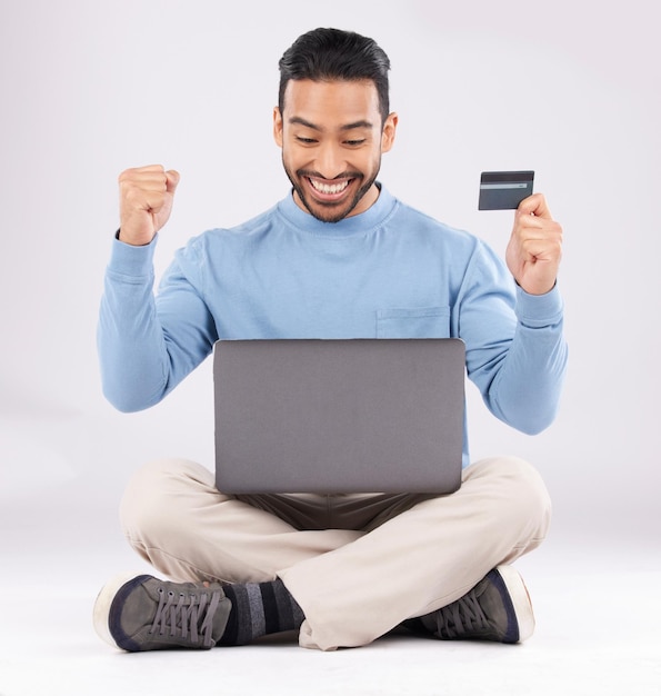 Feierlicher Laptop und asiatischer Mann mit Kreditkarte im Studio aufgeregt für Cashback-Bonus auf grauem Hintergrund Online-Shopping-Werbegeschenk und männlicher Kunde mit guten Nachrichten über Mitgliedschaft oder erfolgreiche Anmeldung