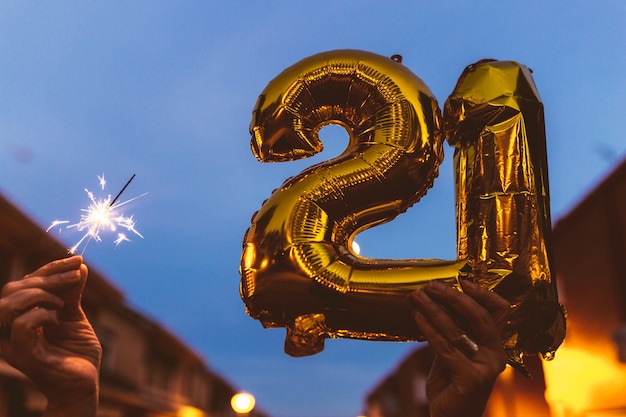 Feiern mit Goldfolienballons Nummer 21 und Wunderkerze in der Nacht. Frohes Neues Jahr 2021 feiern.