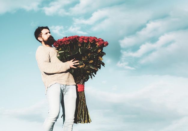 Feiern Sie den Valentinstag Romantische Geschenke und Geschenkideen zum Valentinstag Schöner eleganter Mann hält einen Strauß großer roter Rosen Schöner Mann, der seinem Liebhaber am Valentinstag Blumen schenkt