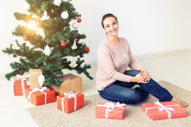 Feiertage, Feiern und festliches Konzept - Schöne junge Frau, die unter Weihnachtsbaum sitzt