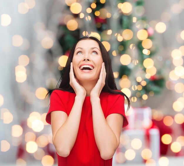 Feiertage, Feiern und Personenkonzept - lächelnde Frau im roten Kleid über Weihnachtsbaumhintergrund