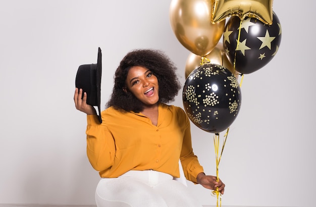Feiertage, Geburtstagsfeier und Spaßkonzept - Porträt der lächelnden jungen afroamerikanischen jungen Frau, die auf weißem Hintergrund mit Luftballons stilvoll aussieht.