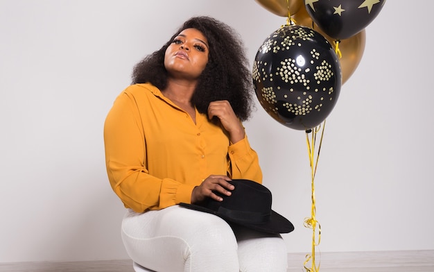 Feiertage, Geburtstagsfeier und Spaßkonzept - Porträt der lächelnden jungen afroamerikanischen jungen Frau, die auf weißem Hintergrund mit Luftballons stilvoll aussieht.