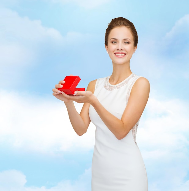 Feiertage, Geschenke, Hochzeit und Glückskonzept - lächelnde Frau in weißem Kleid mit roter Geschenkbox über blauem Hintergrund des bewölkten Himmels