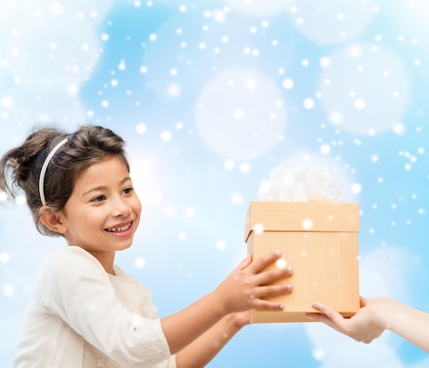 feiertage, geschenke, weihnachten, kindheit und personenkonzept - lächelndes kleines mädchen mit geschenkbox über blaulichthintergrund