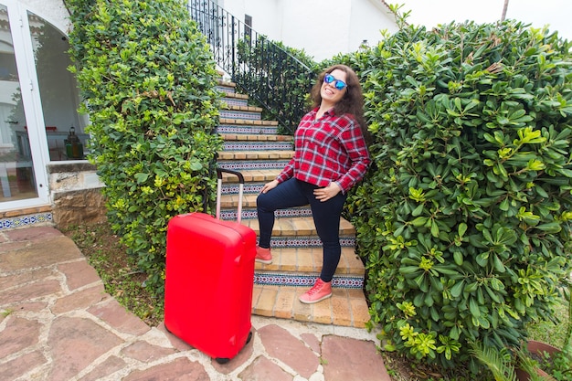 Feiertage, Reisen, Personenkonzept - junge Frau in der Sonnenbrille, die auf Treppen mit Koffern steht und lächelt