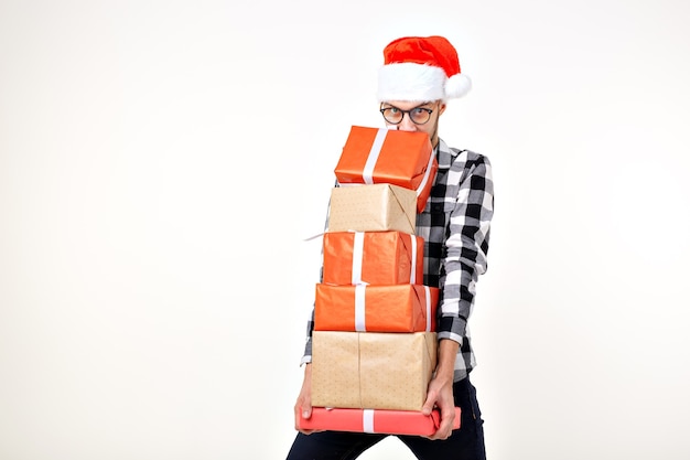 Feiertage und Geschenke Konzept - Lustiger Mann in Weihnachtsmütze mit vielen Geschenkboxen auf weißem Hintergrund