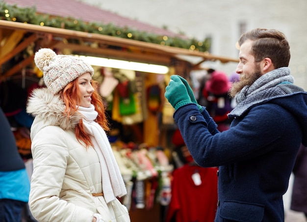 Feiertage, Winter, Weihnachten, Technologie und Personenkonzept - glückliches Touristenpaar in warmer Kleidung, das mit dem Smartphone oder der Kamera in der Altstadt fotografiert